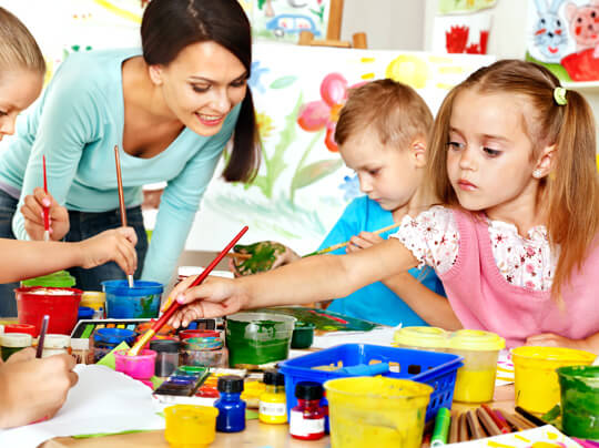 A group of children are painting at a table with a teacher.