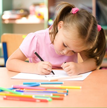 A little girl is drawing with colored pencils in a classroom.