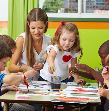 A group of children are painting at a table with a teacher.