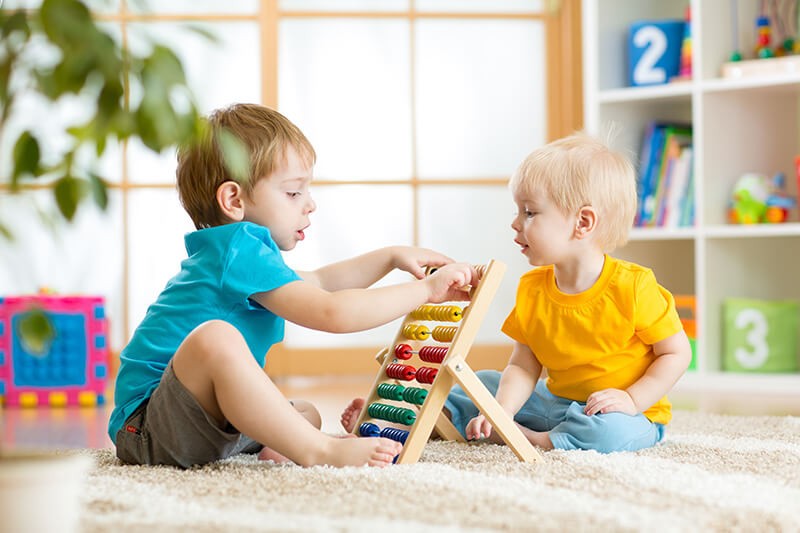 Two children playing with an abacus in a room.