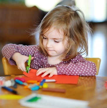 A little girl is making crafts at a table.