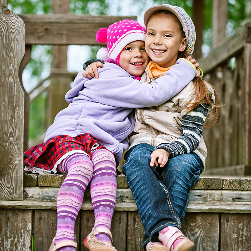 Two little girls hugging each other on a wooden bench.
