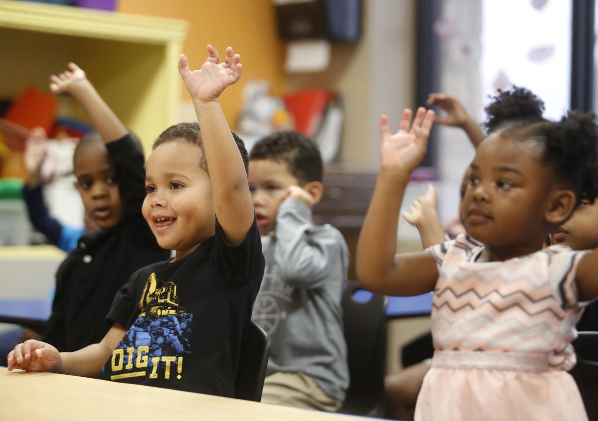 A group of children in a classroom raising their hands.