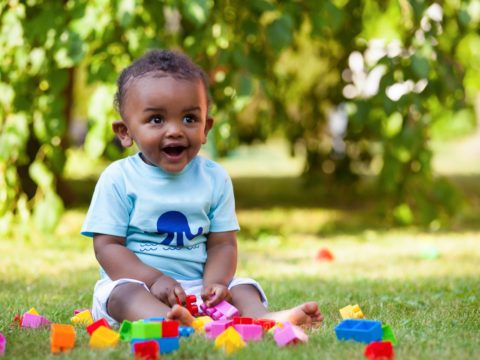 A baby boy playing with blocks in the grass.