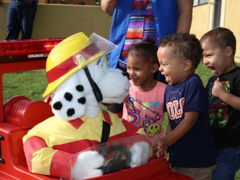 A group of children play with a fire truck stuffed animal.